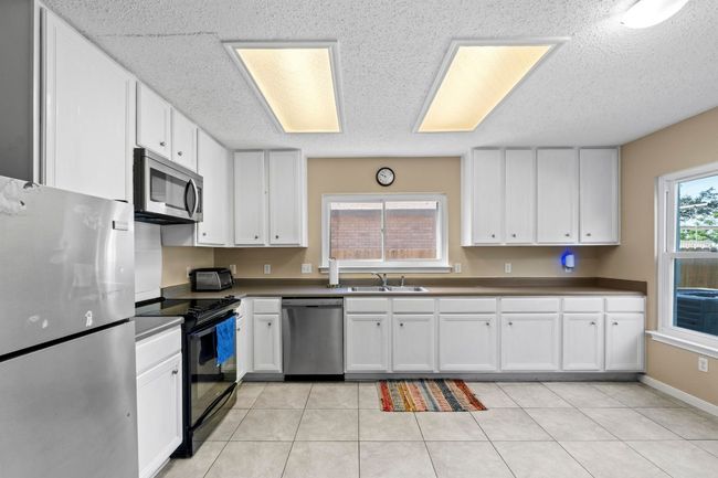 Kitchen with appliances with stainless steel finishes, a sink, a textured ceiling, white cabinets, and dark countertops | Image 12