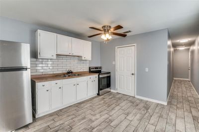 Kitchen with white cabinets, tasteful backsplash, appliances with stainless steel finishes, light wood-type flooring, and sink | Image 1