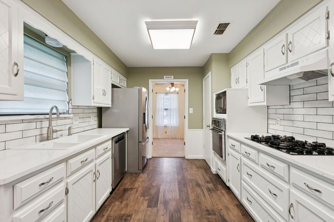 Kitchen featuring black appliances, under cabinet range hood, white cabinets, wainscoting, and tasteful backsplash | Image 11