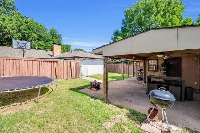 Fenced backyard featuring a trampoline, an outdoor fire pit, a patio, and ceiling fan | Image 19