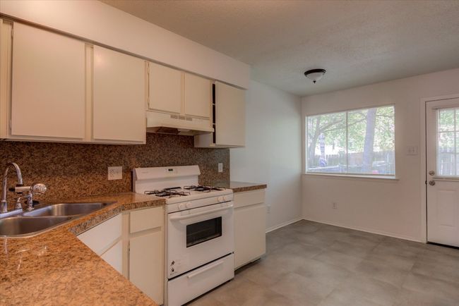 Kitchen with white range with gas stovetop, under cabinet range hood, a sink, and decorative backsplash | Image 8