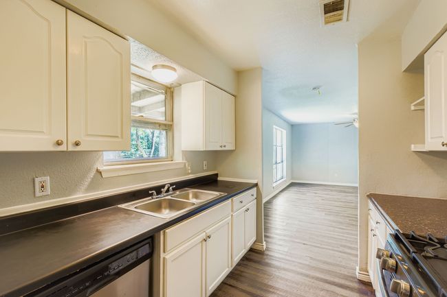 Kitchen featuring dark countertops, wood finished floors, dishwasher, gas range oven, and white cabinets | Image 4