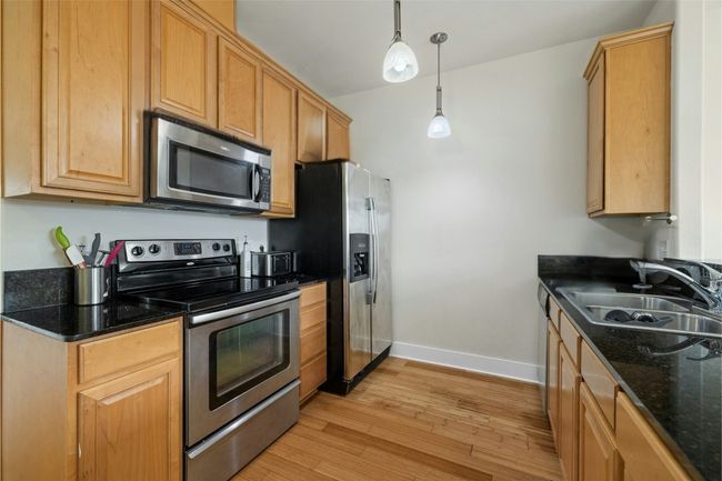 Kitchen featuring light wood-style flooring, appliances with stainless steel finishes, a sink, hanging light fixtures, and baseboards | Image 4