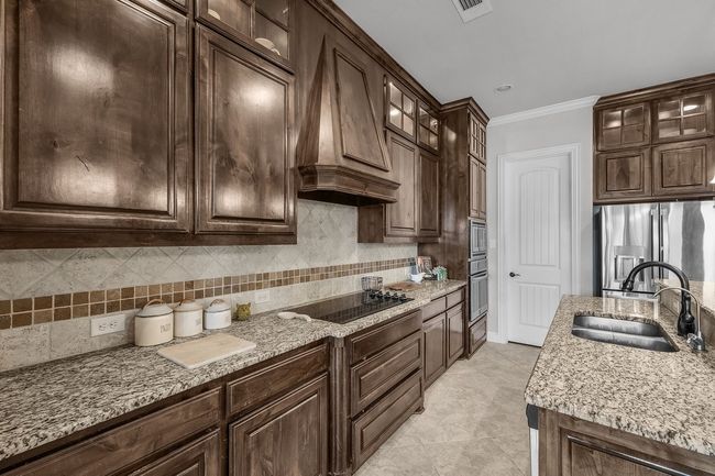 Kitchen featuring a sink, stainless steel appliances, custom exhaust hood, light stone counters, and crown molding | Image 21