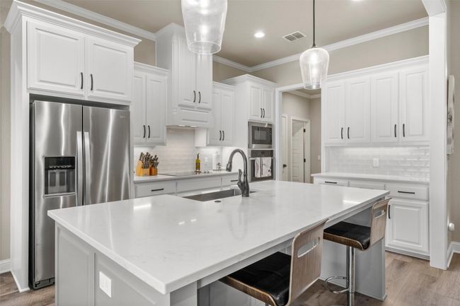 Kitchen with an island with sink, light wood-style flooring, ornamental molding, visible vents, and stainless steel appliances | Image 8
