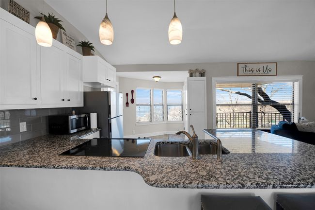 Kitchen with appliances with stainless steel finishes, a sink, dark stone counters, white cabinets, and tasteful backsplash | Image 8