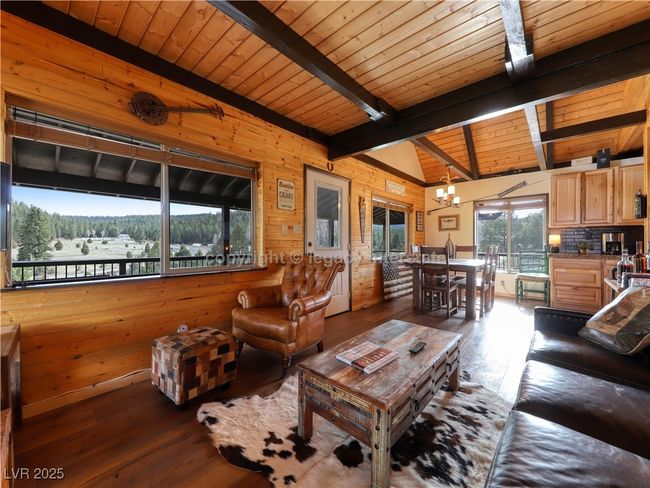 Living area with wood ceiling, wood walls, hardwood / wood-style flooring, a notable chandelier, and vaulted ceiling with beams | Image 10