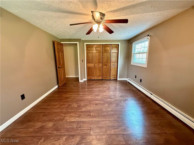 Unfurnished bedroom with a baseboard heating unit, dark wood-style floors, a textured ceiling, and baseboards | Image 30