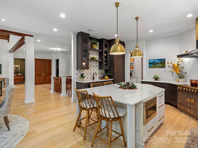 The lit wet bar on the lefts side of the kitchen has decorative wall tile, glass front cabinets, a round porcelain sink and Zephyr wine/beverage refrigerator. The kitchen's Sub-Zero refrigerator/freezer is just to the right of the wet bar. | Image 16