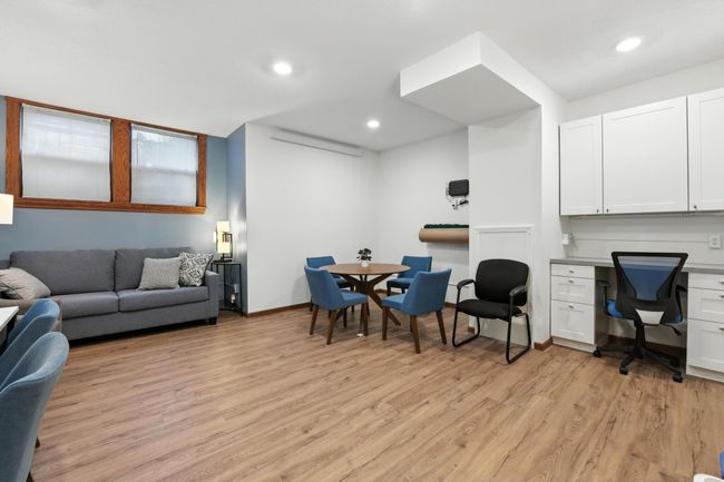 Community space with sofa, dining/game table, workstations, and wood-look flooring. | Image 28