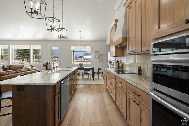 Kitchen with a center island with sink, a notable chandelier, decorative backsplash, appliances with stainless steel finishes, and a breakfast bar area | Image 10