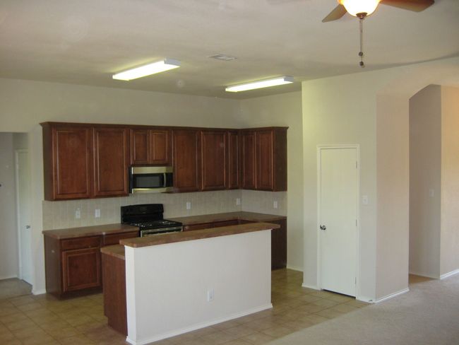 Kitchen with stainless steel microwave, range with electric stovetop, arched walkways, tasteful backsplash, and a ceiling fan | Image 6