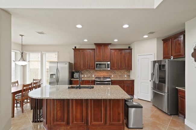 This spacious kitchen features elegant dark wood cabinets, granite countertops, and stainless steel appliances. An island provides extra workspace, while the adjacent dining area offers ample natural light through large windows. (Refrigerators do not convey). | Image 14