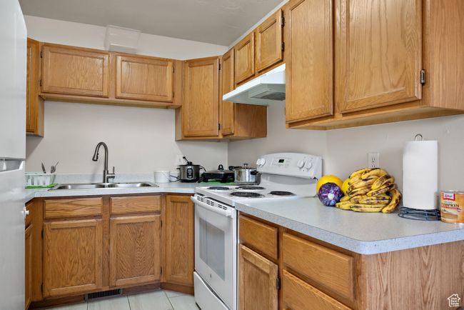 Kitchen with white range with electric stovetop, under cabinet range hood, freestanding refrigerator, light countertops, and brown cabinetry | Image 26
