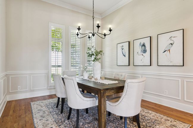 The freshly painted dining room boasts updated light fixture, wood flooring, crown moulding, wainscoting, and plantation shutters. | Image 7