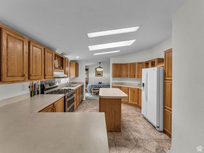 Kitchen with stainless steel appliances, a skylight, a sink, under cabinet range hood, and light countertops | Image 9