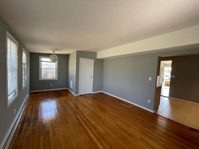 Empty room featuring a baseboard radiator, wood finished floors, an inviting chandelier, and baseboards | Image 6