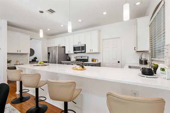 Kitchen with visible vents, a sink, a peninsula, wood finished floors, and stainless steel appliances | Image 13