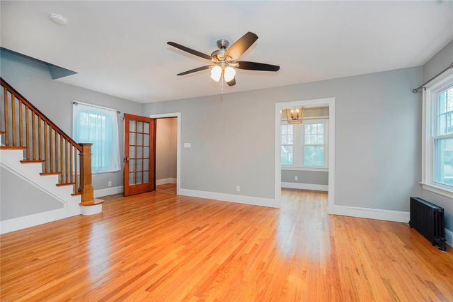 Unfurnished living room featuring radiator heating unit, plenty of natural light, light wood finished floors, and ceiling fan with notable chandelier | Image 4