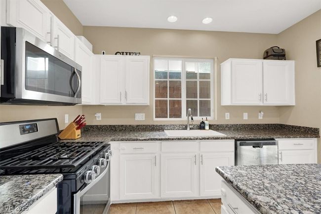 Kitchen featuring appliances with stainless steel finishes, a sink, dark stone countertops, white cabinetry, and light tile patterned flooring | Image 9