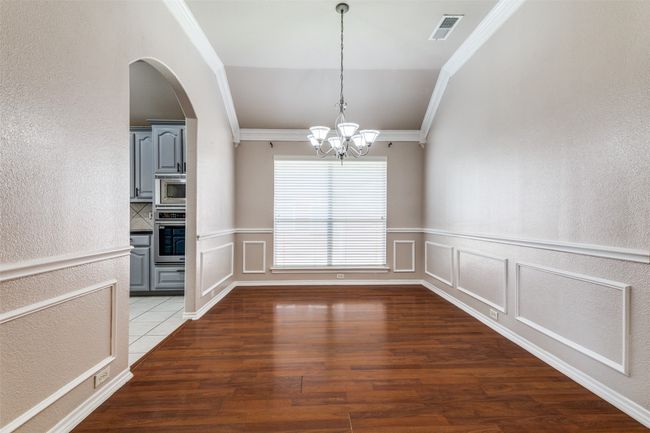 Unfurnished dining area with crown molding, a chandelier, light wood-style flooring, a wainscoted wall, and arched walkways | Image 8