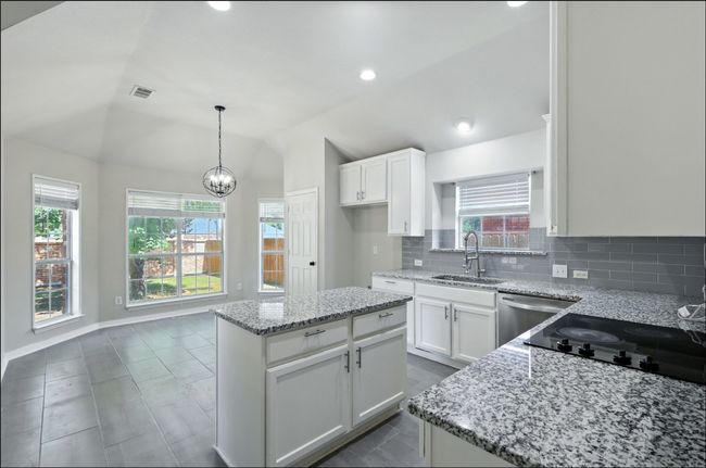 Kitchen with light stone countertops, white cabinetry, backsplash, vaulted ceiling, and a center island | Image 19