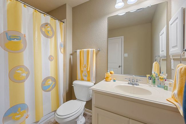 Bathroom with a shower with shower curtain, toilet, a textured wall, and vanity | Image 8
