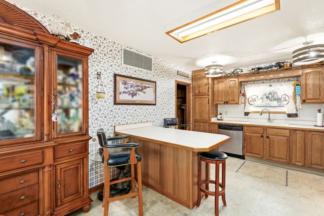 Kitchen with light countertops, a kitchen bar, wallpapered walls, a sink, and stainless steel dishwasher | Image 44