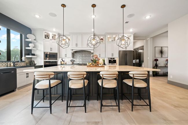 This modern kitchen features a spacious island with seating, stylish pendant lighting, and sleek cabinetry. Large windows provide natural light, while stainless steel appliances and a decorative backsplash add a touch of elegance. Perfect for cooking and entertaining. | Image 16