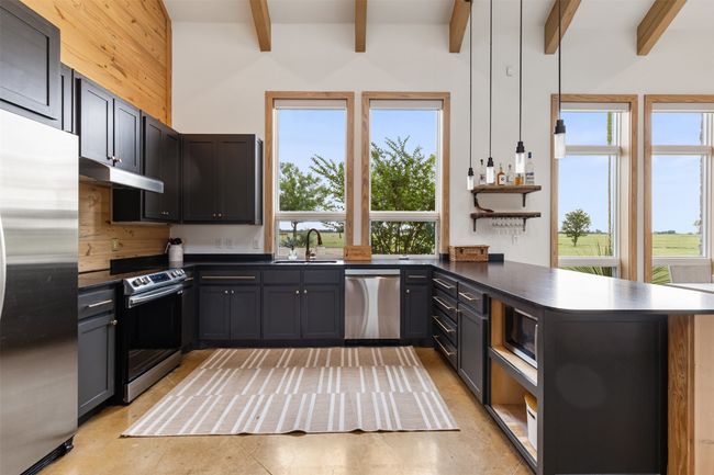 Kitchen featuring appliances with stainless steel finishes, a peninsula, beamed ceiling, dark countertops, and under cabinet range hood | Image 12