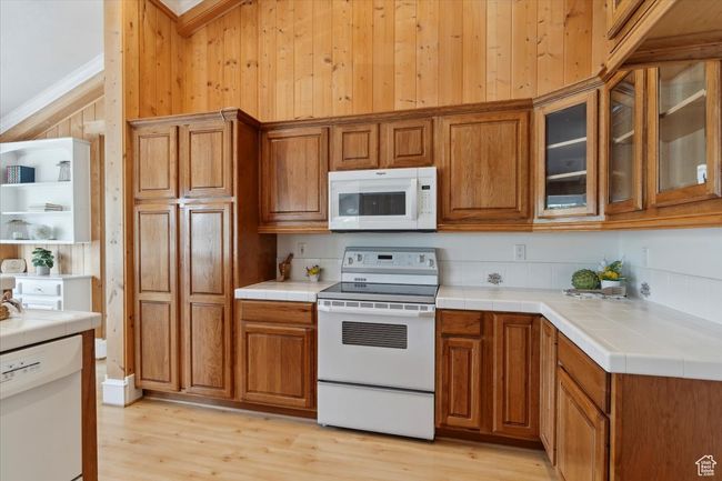 Kitchen featuring white appliances, brown cabinets, tile countertops, light wood finished floors, and wood walls | Image 11