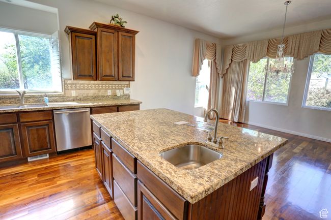 Kitchen featuring wood-type flooring, stainless steel dishwasher, a sink, and an island with sink | Image 23