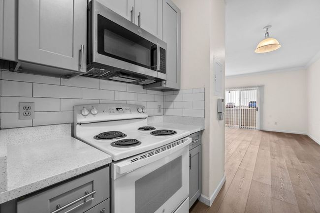 Kitchen with white electric range, stainless steel microwave, gray cabinets, tasteful backsplash, and baseboards | Image 5