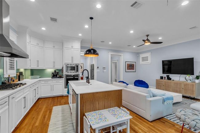 This open-concept living space features a gourmet kitchen with white cabinetry, stainless steel appliances, and an oversized island with a sink. It seamlessly connects to the family room and the breakfast room (currently used as a play room). | Image 11
