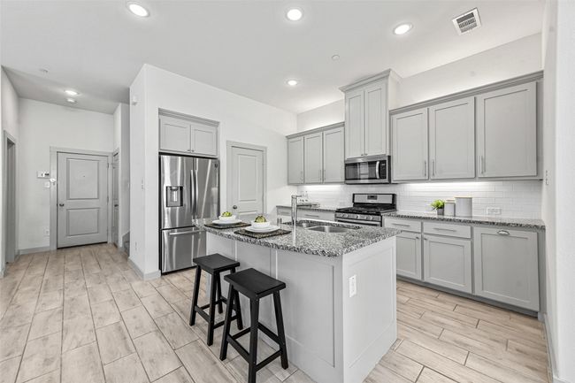 Kitchen featuring light stone counters, sink, an island with sink, and appliances with stainless steel finishes | Image 17