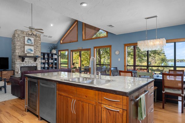 Kitchen with light hardwood / wood-style floors, a kitchen island with sink, wine cooler, ceiling fan with notable chandelier, and sink | Image 14