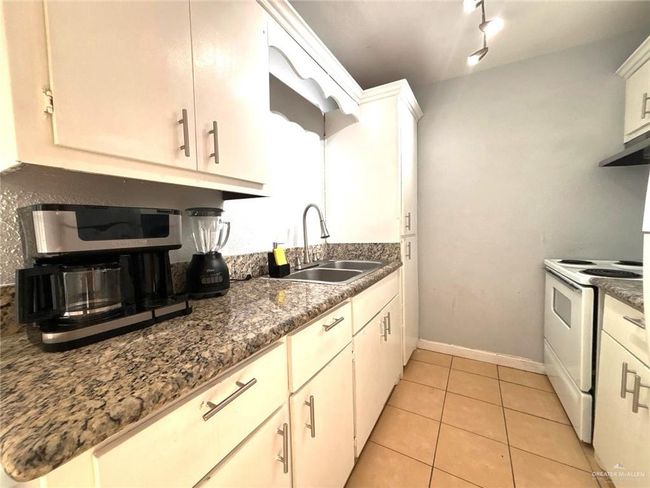 Kitchen with baseboards, white electric stove, dark countertops, light tile patterned flooring, and a sink | Image 9