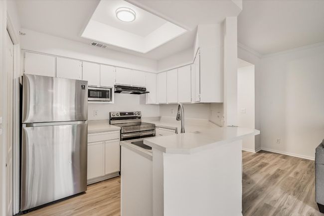 Kitchen with appliances with stainless steel finishes, under cabinet range hood, light countertops, a peninsula, and white cabinets | Image 5