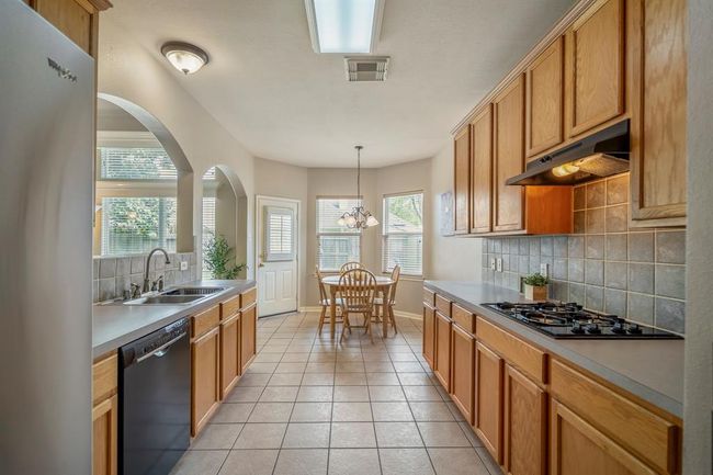 From near the fridge and pantry, looking back down the kitchen towards the breakfast nook, you can see the spacious layout, with the counter-height bar opening to the living room, offering a seamless flow between the kitchen and dining areas. | Image 14