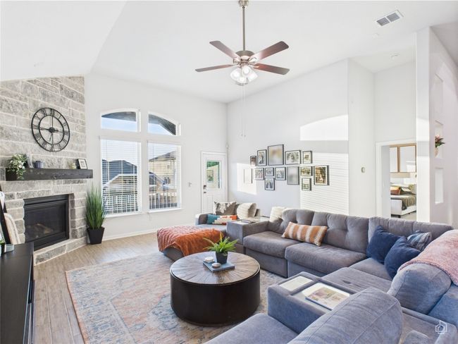 Living area with high vaulted ceiling, a ceiling fan, a stone fireplace, and wood finished floors | Image 16