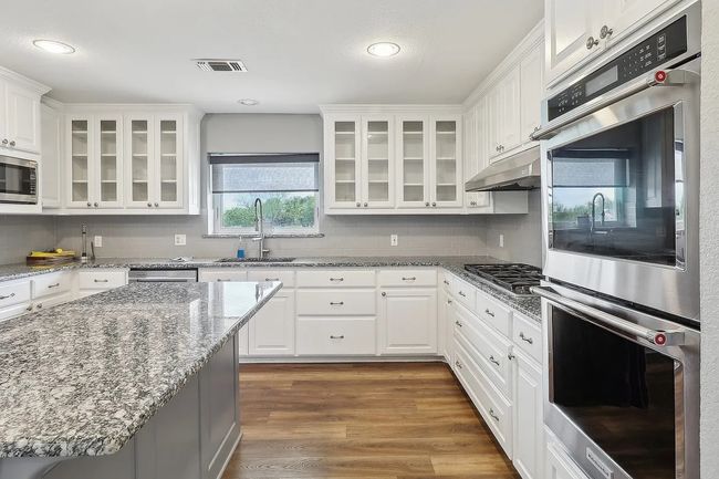 Kitchen featuring dark wood-style flooring, stainless steel appliances, under cabinet range hood, a sink, and visible vents | Image 9