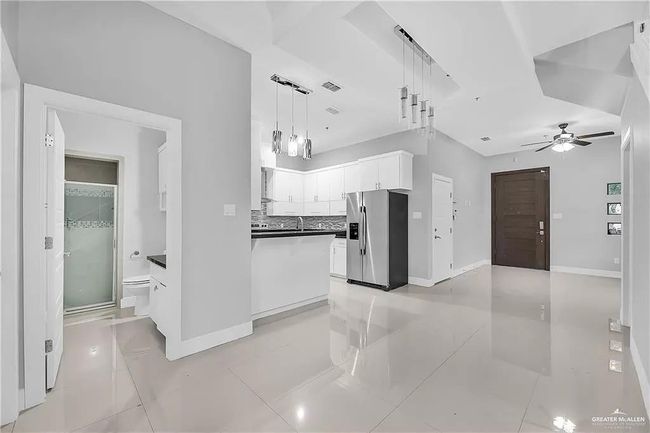 Kitchen featuring stainless steel fridge with ice dispenser, white cabinetry, a ceiling fan, light tile patterned flooring, and tasteful backsplash | Image 5