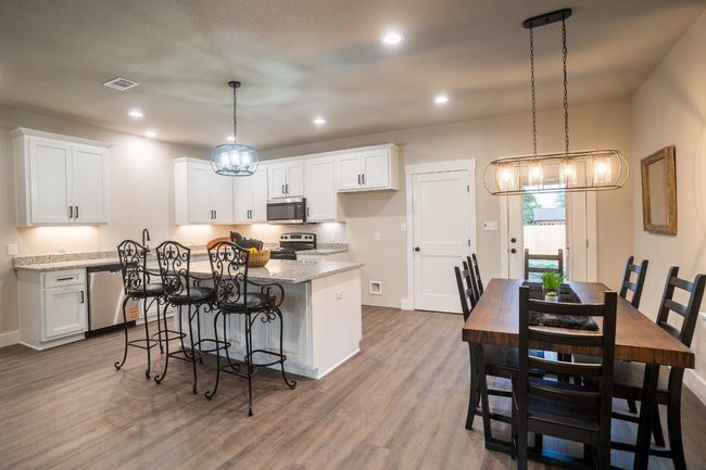 Kitchen with appliances with stainless steel finishes, a center island, white cabinets, wood finished floors, and light stone countertops | Image 5