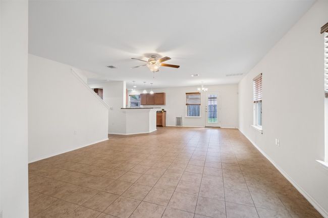 Unfurnished living room with light tile patterned flooring, visible vents, baseboards, and ceiling fan with notable chandelier | Image 11