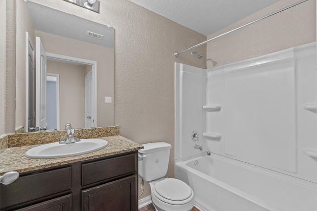 Bathroom featuring a textured wall, washtub / shower combination, vanity, toilet, and visible vents | Image 17