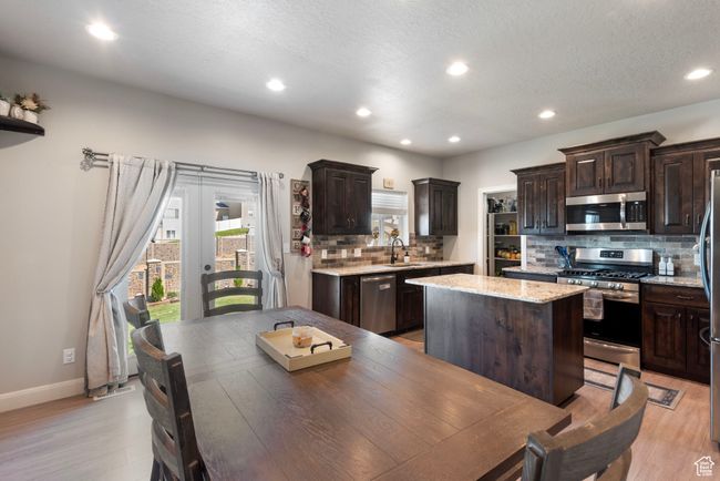 Kitchen with dark brown cabinetry, light wood finished floors, a kitchen island, stainless steel appliances, and a sink | Image 6