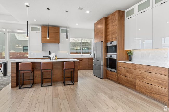 Kitchen featuring a kitchen breakfast bar, light countertops, backsplash, modern cabinets, and brown cabinetry | Image 10