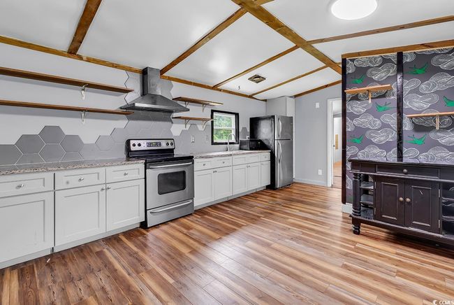Kitchen featuring appliances with stainless steel finishes, exhaust hood, open shelves, backsplash, and a wood stove | Image 4