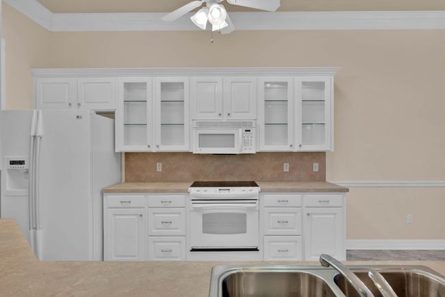 Kitchen with white appliances, crown molding, light countertops, a ceiling fan, and white cabinetry | Image 9