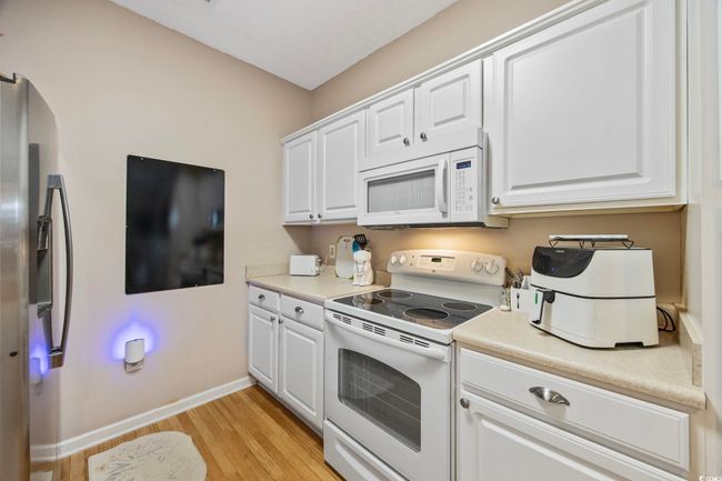 Kitchen with white appliances, light wood-style flooring, white cabinets, baseboards, and light countertops | Image 9